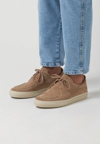 Lichtbruine suède sneakers met een ronde neus, vetersluiting en een crèmekleurige rubberen zool. Gecombineerd met opgerolde lichtblauwe jeans.