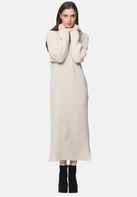 Helles beiges, geripptes Strickkleid mit gerader Silhouette und langen Ärmeln, das über einen hohen Halsausschnitt und einen leicht fransigen Saum verfügt.