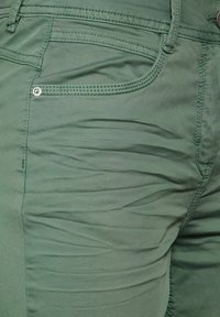 Pantalones verde oliva con una textura suave, costuras visibles y un botón de metal. Incluyen bolsillos frontales con un diseño elegante.