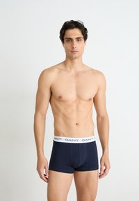 Marineblauwe aansluitende boxershorts met een witte elastische tailleband waarop het "GANT" logo staat. Gladde katoen stof, minimalistisch ontwerp, middelhoge snit.