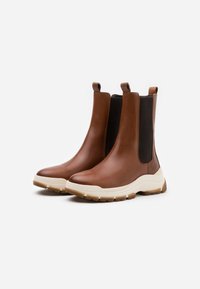 Bottines en cuir marron avec panneaux latéraux élastiques et languettes de tirage, dotées d'une semelle extérieure blanche épaisse et d'accents beiges texturés.