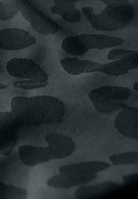 Svart tyg med en texturerad, matt yta som har ett subtilt mörkt leopardmönster. Designen framhäver oregelbundna former genom hela tyget.