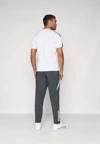 Camisetta bianca a maniche corte abbinata a pantaloni sportivi grigio scuro con strisce bianche, progettata con una vestibilità comoda e una texture liscia.