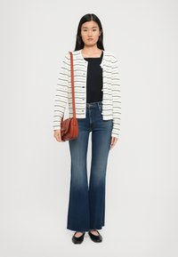 Cardigan bianco con motivo a righe orizzontali, abbinato a una maglietta nera e jeans blu a campana. Gli accessori includono una piccola borsa a tracolla marrone.