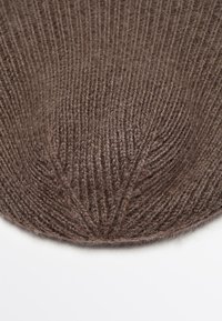 Berretto lavorato a maglia marrone, con una textura a coste e una cima arrotondata. Il materiale sembra morbido e caldo, con sottili variazioni di tono.