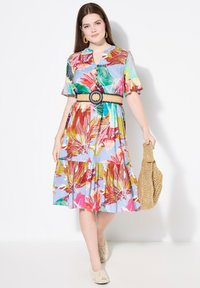 Vestido de estampado floral con mangas cortas, escote abotonado y falda de volantes. Accesorios incluyen un cinturón ancho de tejido y un bolso de paja.