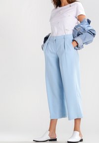 Světle modré kalhoty s širokými nohavicemi a sklady, spárované s bílým tričkem s metalickými akcenty a džínovou bundou. Bílé nazouvací boty.