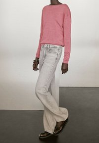 Long-sleeve coral shirt paired with light gray wide-leg jeans and black flip-flops. Simple design with minimal detailing.