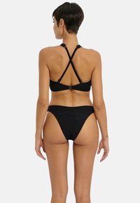 Black bikini set made of textured fabric. Top has crisscross straps and adjustable hardware. Bottom features a high-cut design.
