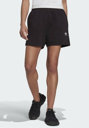 Černé bavlněné šortky s elastickým pasem, s malým bílým logem Adidas na levé nohavici, v kombinaci s černými sportovními botami.