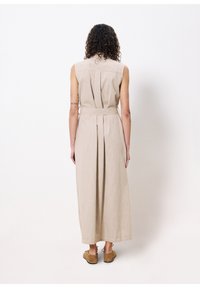 Beige ärmelloses Maxikleid mit gebundenem Taillengürtel, das eine Plisseeverzierung und natürliche Textur aufweist. Schlichter Rücken mit Kragen und Knöpfen ohne Muster.