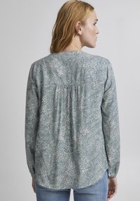 Blusa azzurro chiaro con motivo, a maniche lunghe, caratterizzata da un design posteriore plissettato e polsini elastici. Tessuto morbido con stampa floreale astratta in bianco.