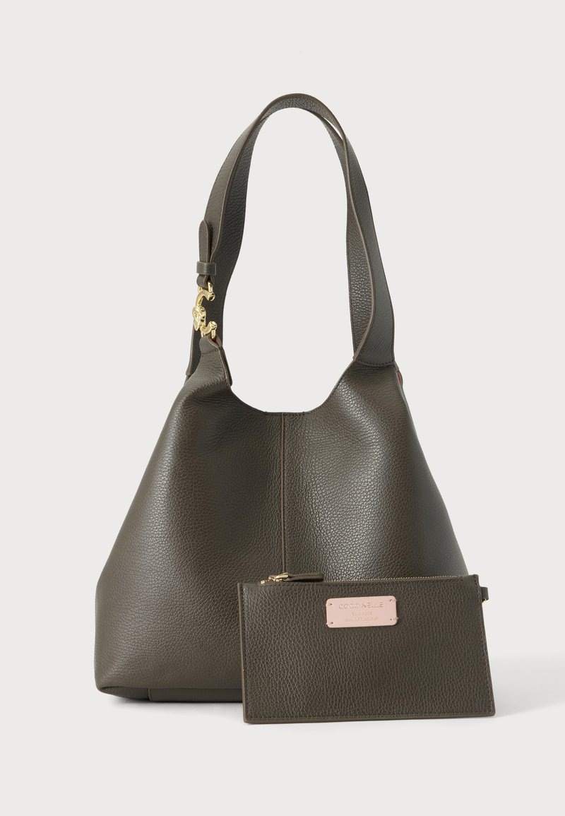 Sac à main en cuir texturé vert foncé avec une large bandoulière et une petite pochette zippée assortie avec une étiquette rose clair à l'avant.