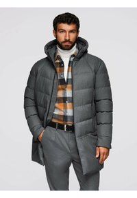 Giacca a vento grigia con cappuccio, caratterizzata da sezioni trapuntate orizzontali. Abbinata a una camicia a quadri nei toni del marrone, grigio e arancione.