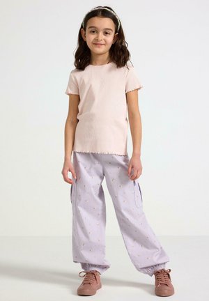 Maglietta corta rosa chiaro a coste con orli scallop, abbinata a pantaloni cargo lilla con un motivo floreale e polsini elastici, indossata con sneakers rosa.