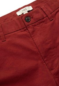 Pantaloni di cotone rossi con un bottone nero, dettagli cuciti e un'etichetta con la scritta "M&S" sulla cintura. Tessuto liscio.