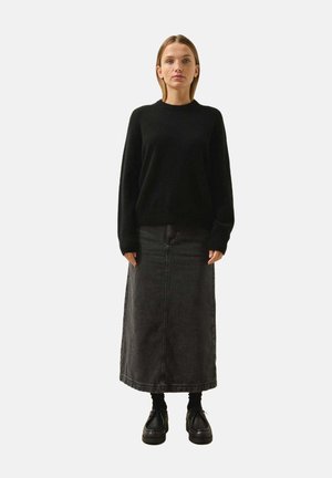 Maglione nero a maglia, con collo alto, abbinato a una gonna midi in denim grigio scuro. Il modello indossa scarpe nere e calze, in piedi su uno sfondo bianco.