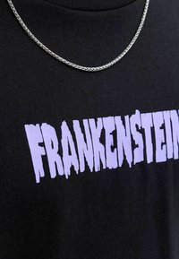 Černé bavlněné tričko s nápisem "FRANKENSTEIN" v kapající fialové barvě, doplněné stříbrným řetízkem.