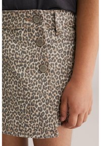 Gonna di jeans con fantasia leopardata, dotata di quattro bottoni in bronzo, taglio dritto e orlo rifinito, mostrata accanto a una mano.