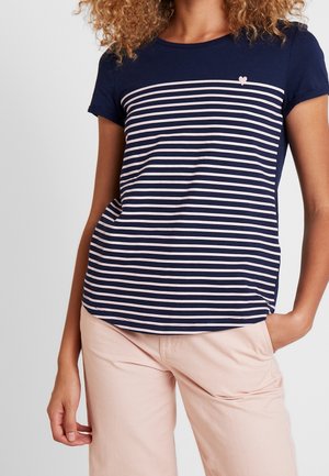 Kvinde iført en mørkeblå og hvid t-shirt med vandrette striber og et lille hjerte-detalje, kombineret med lyserøde bukser.