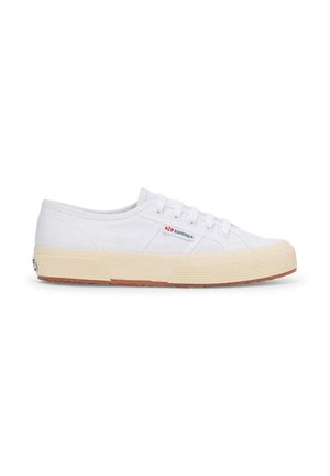 Sneakers bianchi in tela con profilo basso, dotati di una suola in gomma testurizzata, design con lacci e un piccolo logo sul lato.