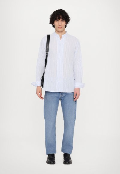 Hvit skjorte med blå striper, lange ermer. Kombinert med lyseblå jeans og svarte sko. Modellen holder en svart bag.