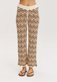 Dzianinowe spodnie o szerokich nogawkach, z beżową bazą ozdobioną wielokolorowymi wzorami w zygzak. Elastyczny pasek w talii z detalem sznurka. Płaskie sandały.