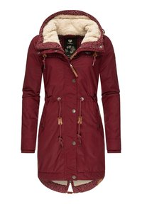 Jacca lungo marrone con interno in peluche, vita regolabile con cordino, doppie tasche laterali e un rivestimento della cappuccio decorato. Presenta dettagli in legno.