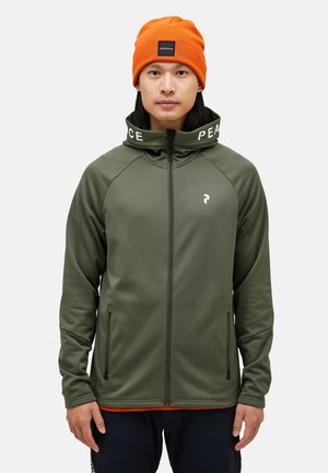 Olive green zip-up jacket with high collar and "PEACE" text. Features raglan sleeves and two side pockets. Worn with an orange beanie.