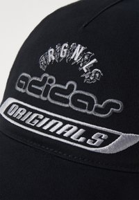 Črna kapa z vezenim logotipom "adidas Originals" v srebrni barvi, z teksturirano tkanino in strukturirano obliko.