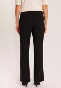 Czarne spodnie o kroju prostym, z dwiema tylnymi kieszeniami i gładką fakturą materiału. Noszone z wysokimi obcasami.