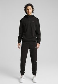 Sudadera de forro polar negra con media cremallera y un pequeño logotipo, combinada con pantalones de chándal negros. Ambos tienen una textura suave y un corte relajado.