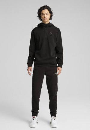 Czarna polarowa bluza z kapturem z pół-zamkiem i małym logo, w zestawie z czarnymi dresami. Oba elementy mają gładką teksturę i luźny krój.