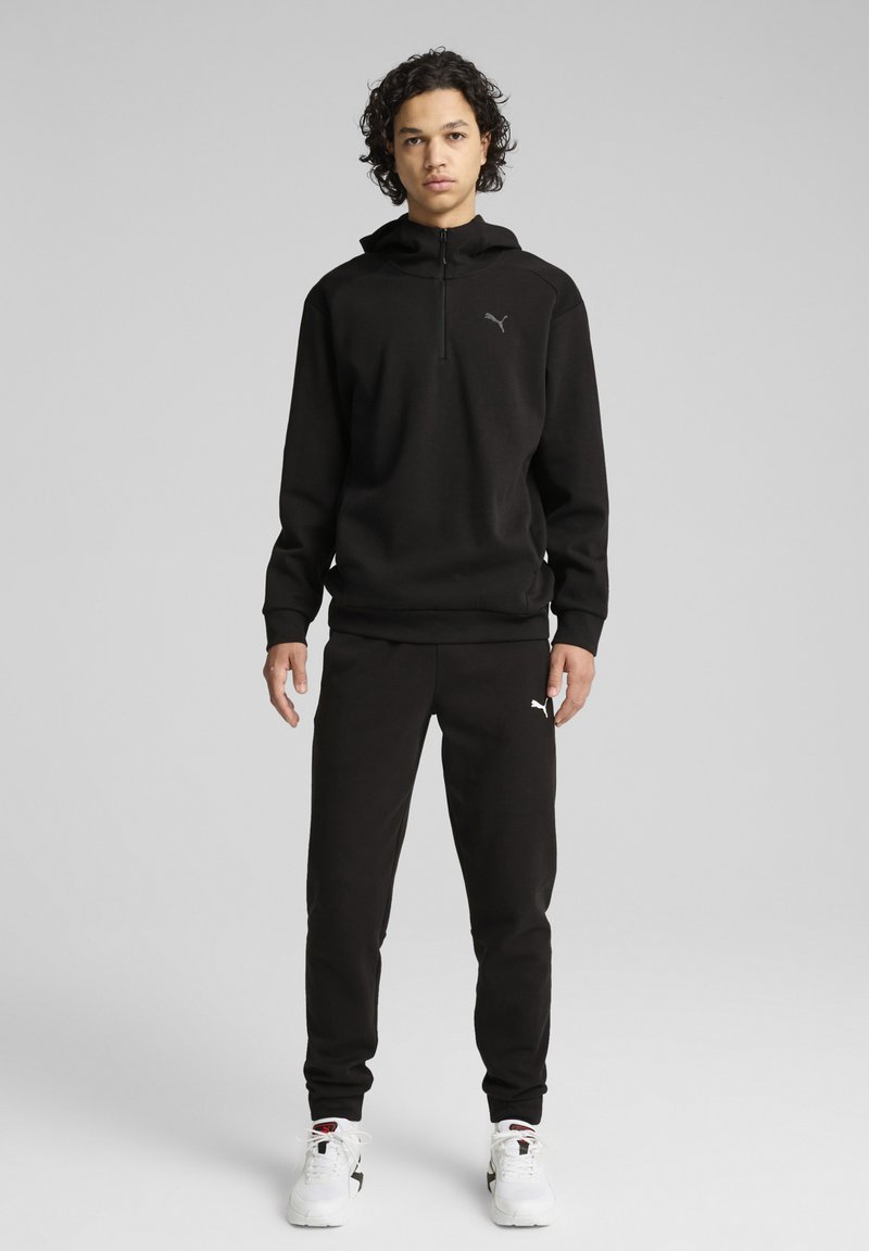 Sudadera de forro polar negra con media cremallera y un pequeño logotipo, combinada con pantalones de chándal negros. Ambos tienen una textura suave y un corte relajado.