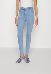 Jeans azzurri a vita alta con una vestibilità slim e tasche laterali, abbinati a tacchi aperti blu con un motivo a logo in rilievo.