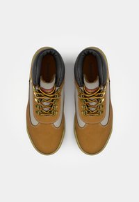 Tan suede boots with grey accents, gold eyelets, and black padded collar. Hexagonal laces and textured interior surface.