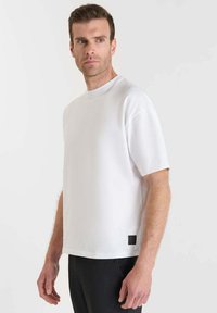 T-shirt bianco a maniche corte realizzato in tessuto liscio, con collo rotondo e un piccolo etichetta nera in basso a sinistra.