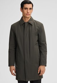 Cappotto verde oliva con colletto a punta, caratterizzato da una linea dritta, maniche lunghe, chiusura frontale nascosta e tasche laterali. Tessuto liscio.