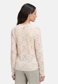 Lange mouwen blouse van kant in lichtbeige, met een bloemenpatroon en een sleutelgatdetail aan de achterkant. Gemaakt met een geruite broek.