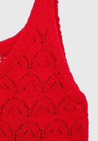 Indumento rosso lavorato a maglia con un motivo triangolare, caratterizzato da un modello aperto e spalline larghe. La texture è morbida e irregolare, con una forma strutturata.
