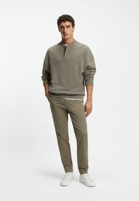 Grå strikket pullover med rund hals og skuldersømme, parret med olivengrønne tapered bukser og hvide sneakers.
