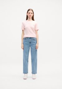 T-shirt rose à manches courtes avec un petit logo, associé à un jean bleu clair taille haute à jambes droites et des baskets blanches avec des accents roses.