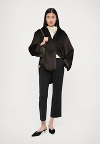 Top in tessuto a costine nero in stile kimono con maniche ampie, abbinato a un dolcevita crema, pantaloni neri aderenti e mule nere. Dettaglio della borsa verde.