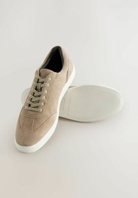 Béžové semišové tenisky s kulatou špičkou, šesti očky na tkaničky a bílou gumovou podrážkou. Minimalistický design bez výrazných vzorů nebo kovových doplňků.