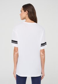 T-shirt bianco a maniche corte con accenti a righe nere sulle maniche, colletto rotondo e vestibilità ampia, realizzato in morbido cotone.
