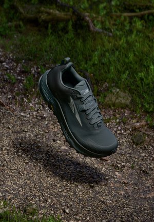 Chaussure de trail running grise avec un upper texturé, un talon renforcé et une semelle robuste, arborant un logo discret et une languette à l'arrière.