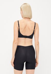 Svart bh med justerbare stropper og krok-lukking; kombinert med høyhalsede svarte shorts, begge har en glatt, sømløs tekstur.