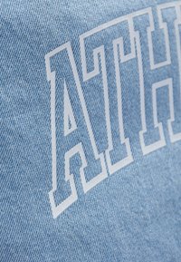 Tissu en denim bleu clair présentant un texte blanc audacieux "ATH". La texture est lisse avec une finition classique légèrement délavée.