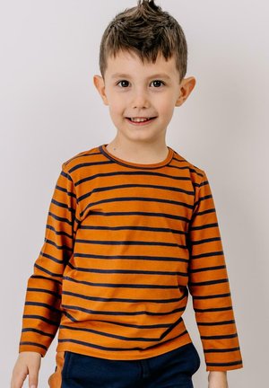 Oranges Langarmshirt mit navyblauen horizontalen Streifen, runder Ausschnitt und weichem Material. Getragen mit dunkelblauen Hosen.