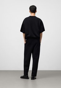 Zwarte oversized top met korte mouwen en taps toelopende broek, beide gemaakt van een zachte stof. Zwarte schoenen met minimale details maken de look compleet.